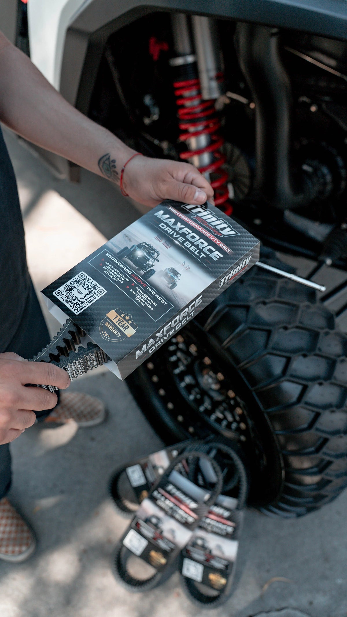 Person holding a MaxTrac product package next to off-road vehicle tires