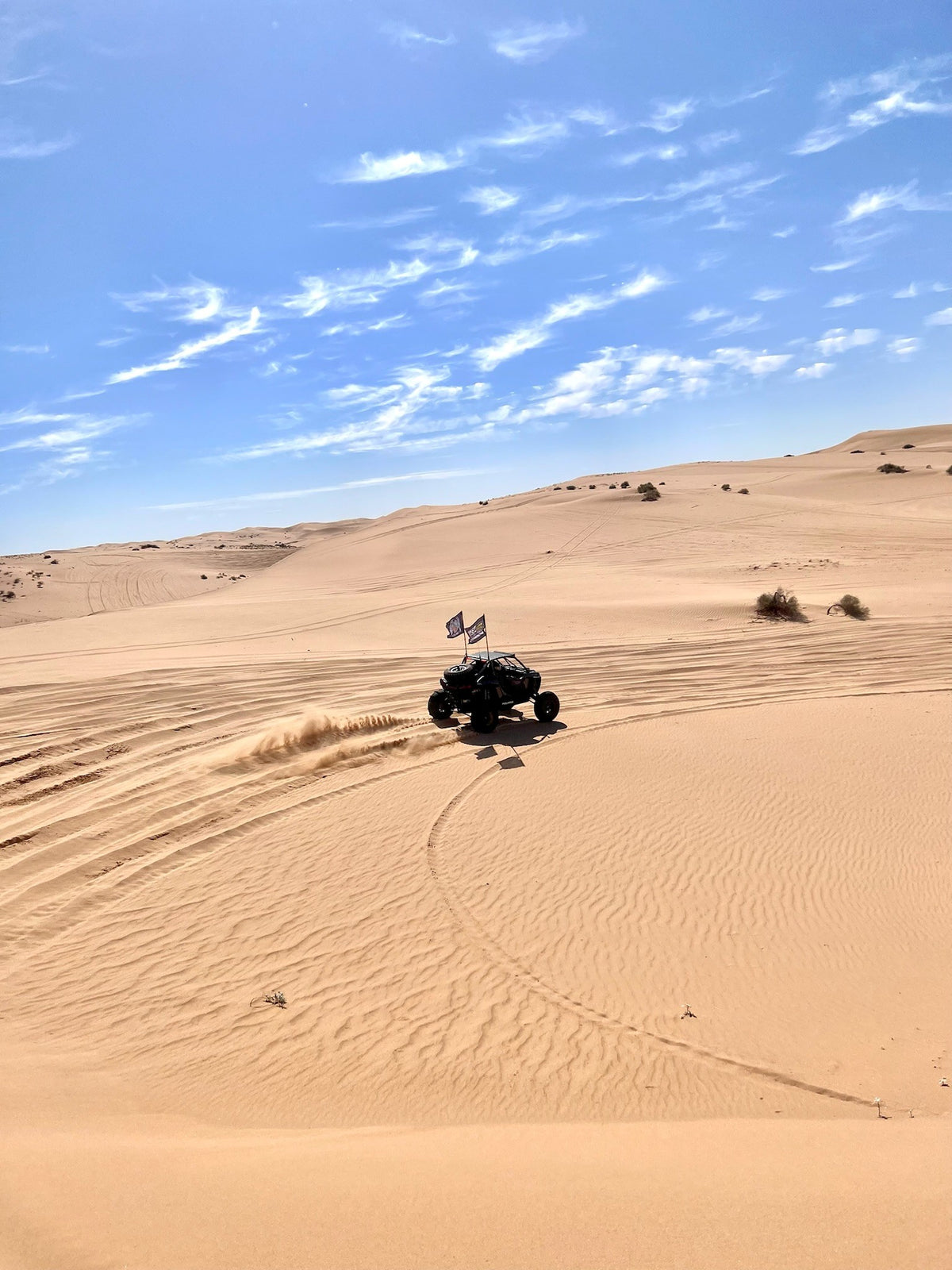 Off-road vehicle driving on sand dunes with a clear blue sky.